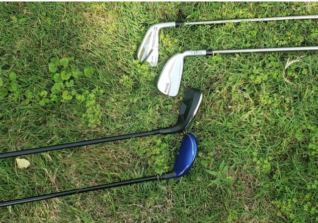 Two regular golf clubs and two hybrid golf clubs laid down on grass