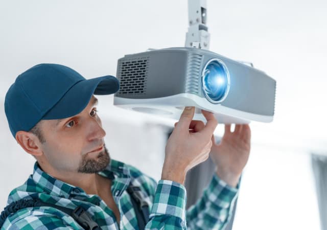 A man fixing the mounting of a ceiling projector.