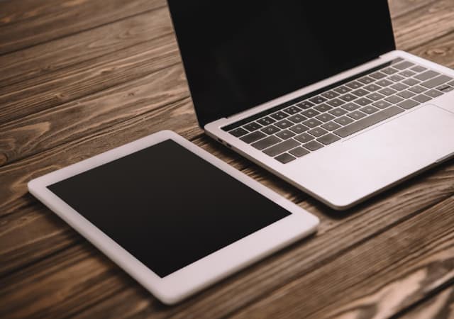 A tablet and a laptop on top of a wooden surface