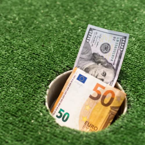 100-dollar and 50-euro bills in a golf hole on artificial grass, symbolizing golf expenses or betting.