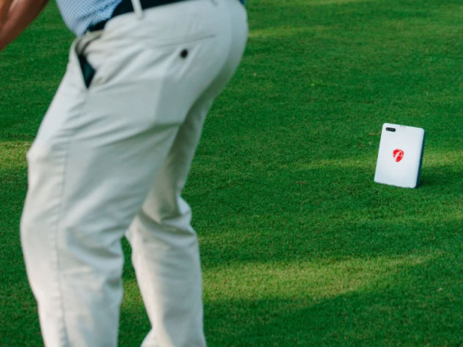Golf swing on a putting green with a golf swing analyzer device in the background for golf simulation and training.