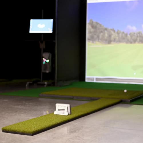 High-tech golf simulator setup in an indoor facility with a large screen displaying a virtual golf course, indoor turf, and launch monitor for realistic golf practice and gameplay.