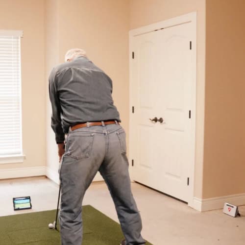 Golf simulator setup in a home interior with an older man preparing for a swing.