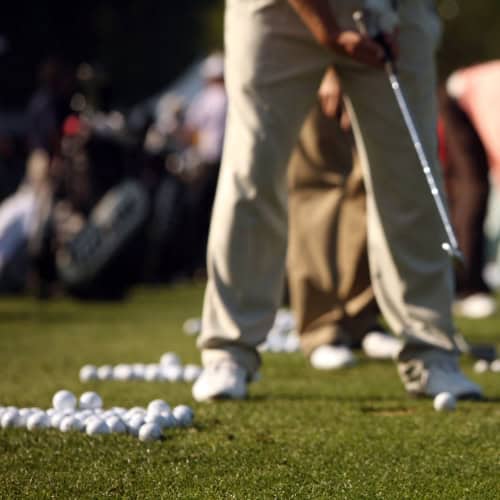 Golf instructor preparing for swing training at an outdoor driving range with numerous golf balls on the green.